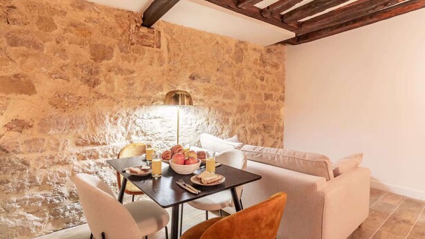 Un comedor acogedor con pared de piedra, techo de madera y una mesa dispuesta con pan, fruta y bebidas.