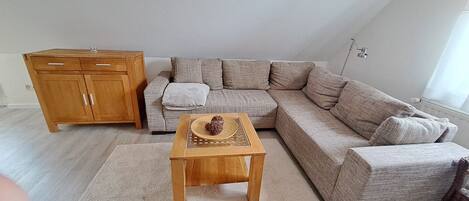 A living room with a wooden cabinet, a beige sectional sofa, and a small wooden table with a decorative item.
