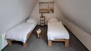 Un dormitorio en ático pequeño y triangular con dos camas individuales, un triciclo de juguete y un cuadro de un faro.