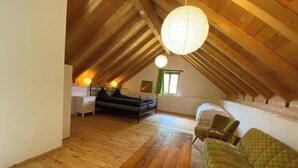 An attic bedroom with a wooden ceiling, a wooden table, a green sofa, and a bed with a green bedspread. - Idyllic country house in Rasa - Centovalli (Centovalli)