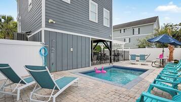A backyard with a swimming pool, lounge chairs, and a patio area.
