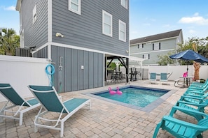 A backyard with a swimming pool, lounge chairs, and a patio area.
