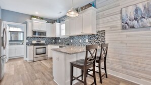 Une cuisine moderne avec des meubles blancs, un îlot central et un revêtement mural composé de carreaux bleus et blancs.