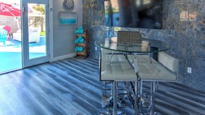 Een moderne keuken met een glazen eettafel, een ingebouwde televisie en een blauwe marmeren achterwand.