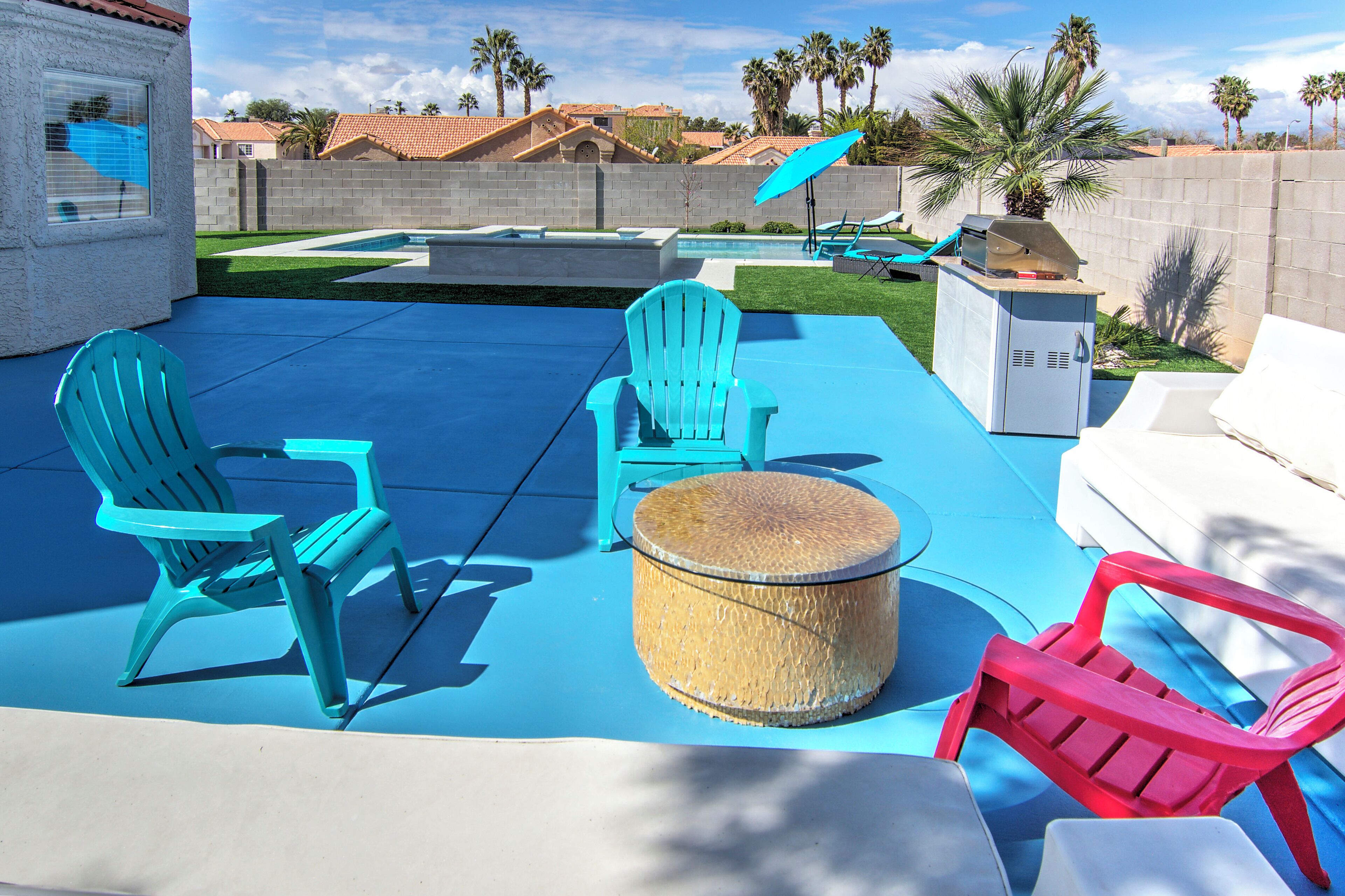 A backyard with a pool, two blue Adirondack chairs, a wicker table, and a red Adirondack chair.
