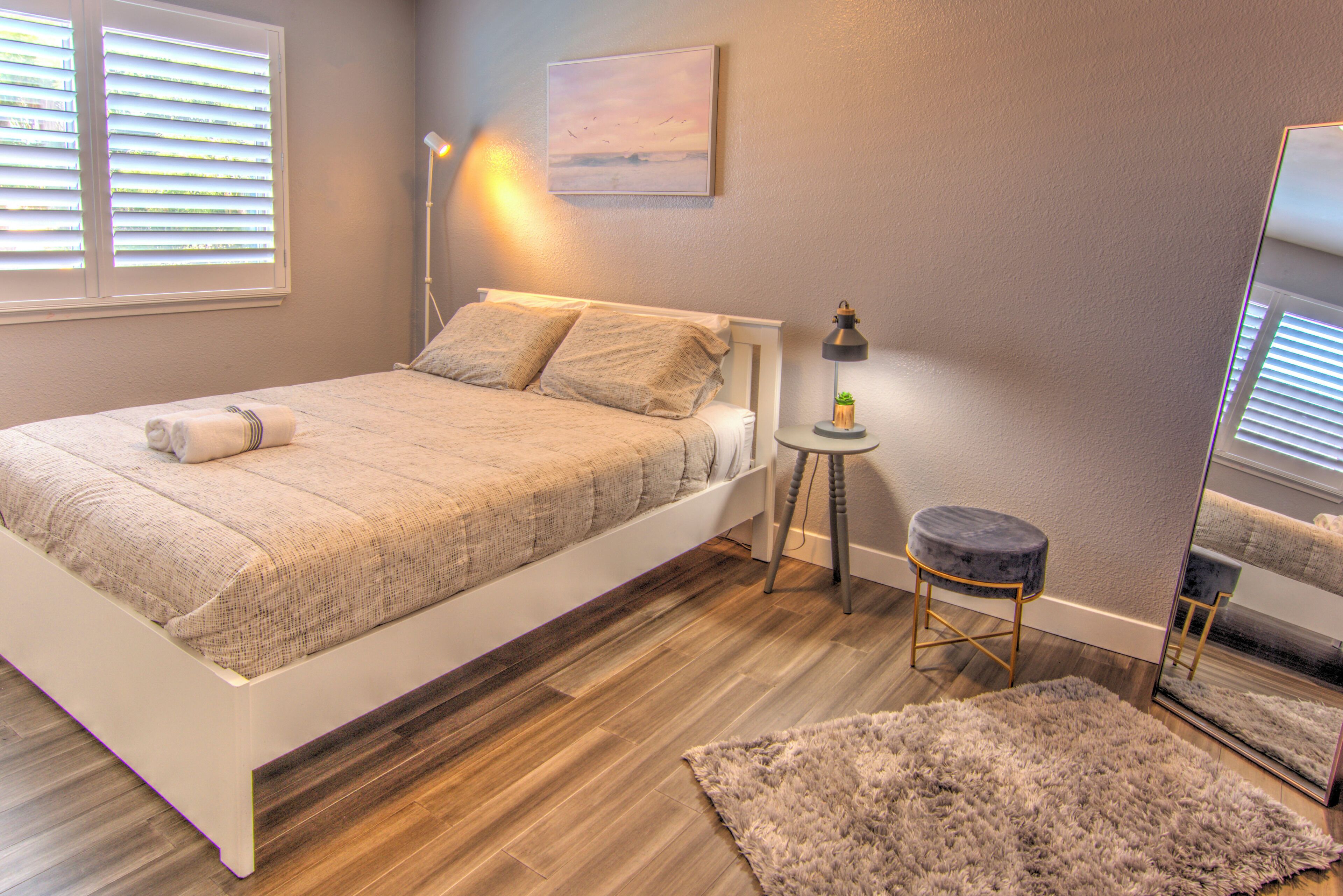 Un dormitorio con cama, mesita de noche, lámpara, espejo y alfombra.