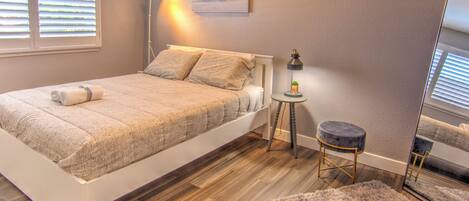 Un dormitorio con cama, mesita de noche, lámpara, espejo y alfombra.