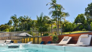 A swimming pool with lounge chairs and a wooden deck. - La Maison Soleil - Modern, sun-filled home with 4 bedrooms (2 kings including a stand-alone sleepout in the pool area, 2 queens) and 3 tiled bathrooms. Features a full kitchen, aircon, and open living flowing to a large garden with BBQ, heated swim s (Waiheke Island)