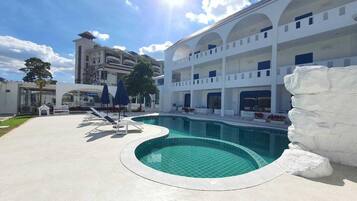 A swimming pool with a white rock feature, surrounded by a white building with multiple balconies and a clear sky.