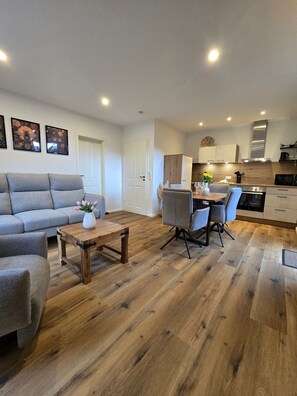 A modern living room with a sofa, a coffee table, and a dining area with chairs and a table. - Holiday Home 'Thiesa' with Private Garden and Wi-Fi (Berumbur)
