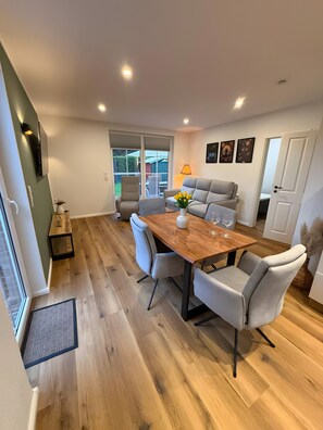 A modern dining area with a wooden table, grey upholstered chairs, and a sofa. - Holiday Home 'Thiesa' with Private Garden and Wi-Fi (Berumbur)