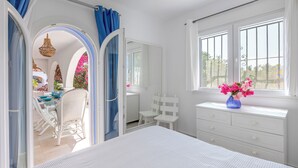 A bedroom with a bed, a dresser, a window with curtains, and a view of an outdoor area with a table and chairs. - Hibiscus by Sun & Sea Homes (Calpe)