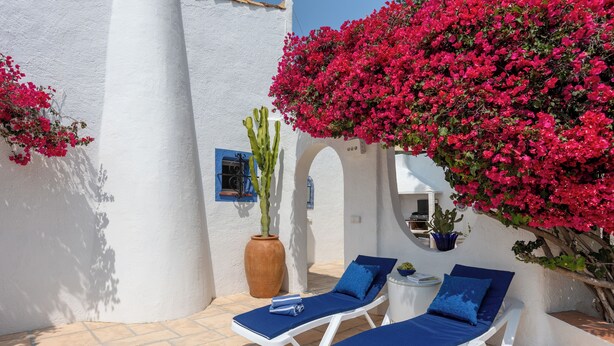 A sunlit outdoor seating area with white lounge chairs and blue cushions, surrounded by white walls and vibrant pink bougainvillea flowers. - Hibiscus by Sun & Sea Homes (Calpe)