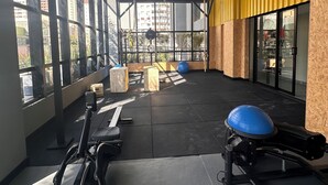 A gym with exercise equipment, large windows, and a yellow accent wall. - 2 Suites Setor Bueno & Vaca Brava Hop Amparo (Goiânia)