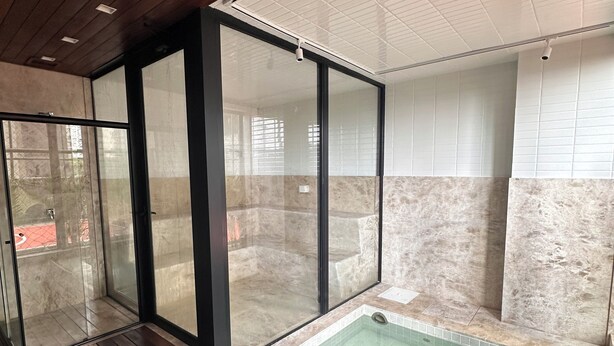 A modern indoor swimming pool with glass walls, wooden deck, and a tiled interior. - 2 Suites Setor Bueno & Vaca Brava Hop Amparo (Goiânia)