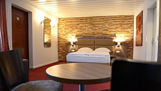 Habitación de hotel con pared de ladrillo, una cama con ropa blanca, dos lámparas de noche, una mesa redonda y dos sillas.