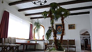 Una habitación con piso de baldosas, muebles de madera, una planta grande en maceta y un cuadro en la pared.