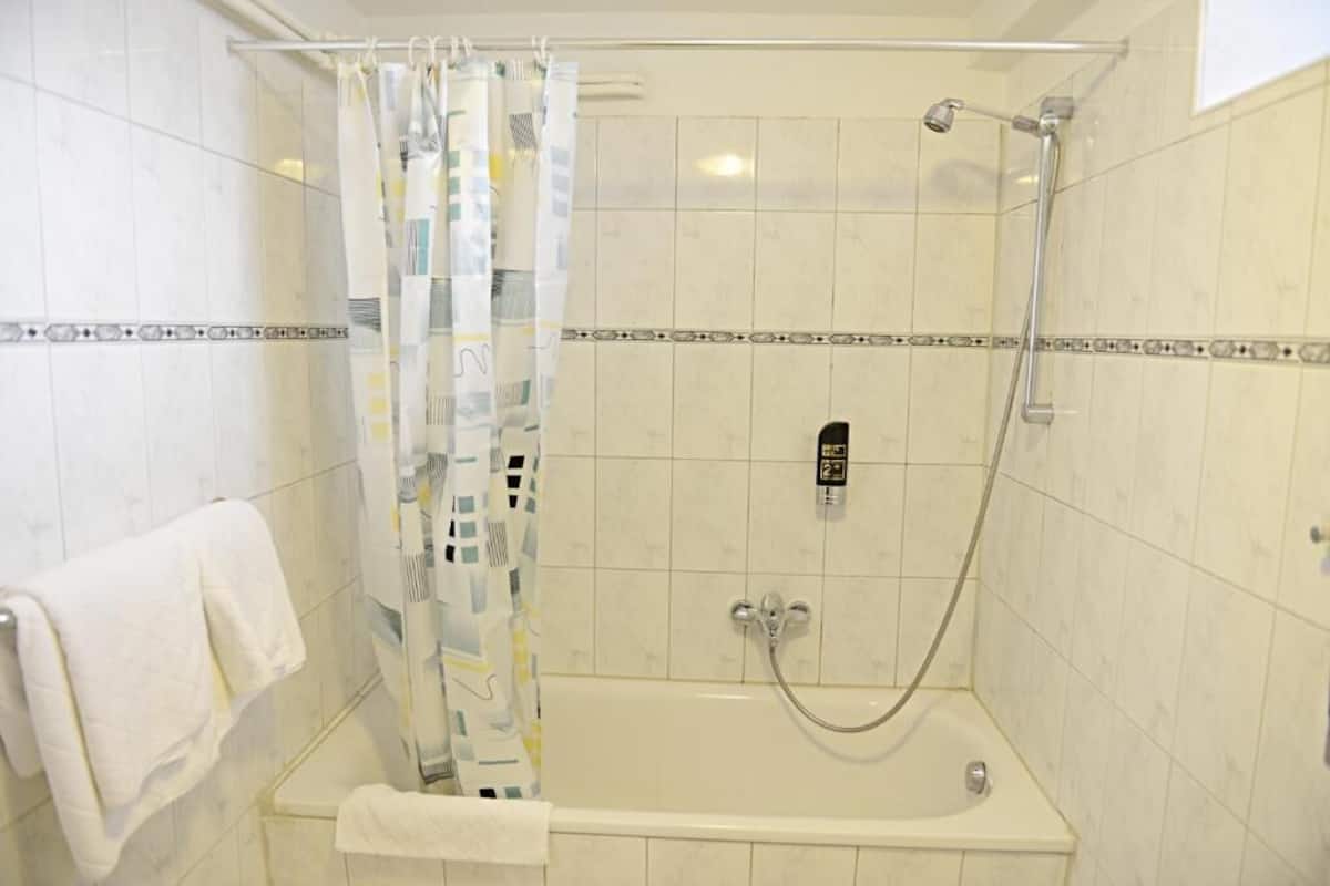 A shower area with a glass door, a handheld showerhead, and a control panel.