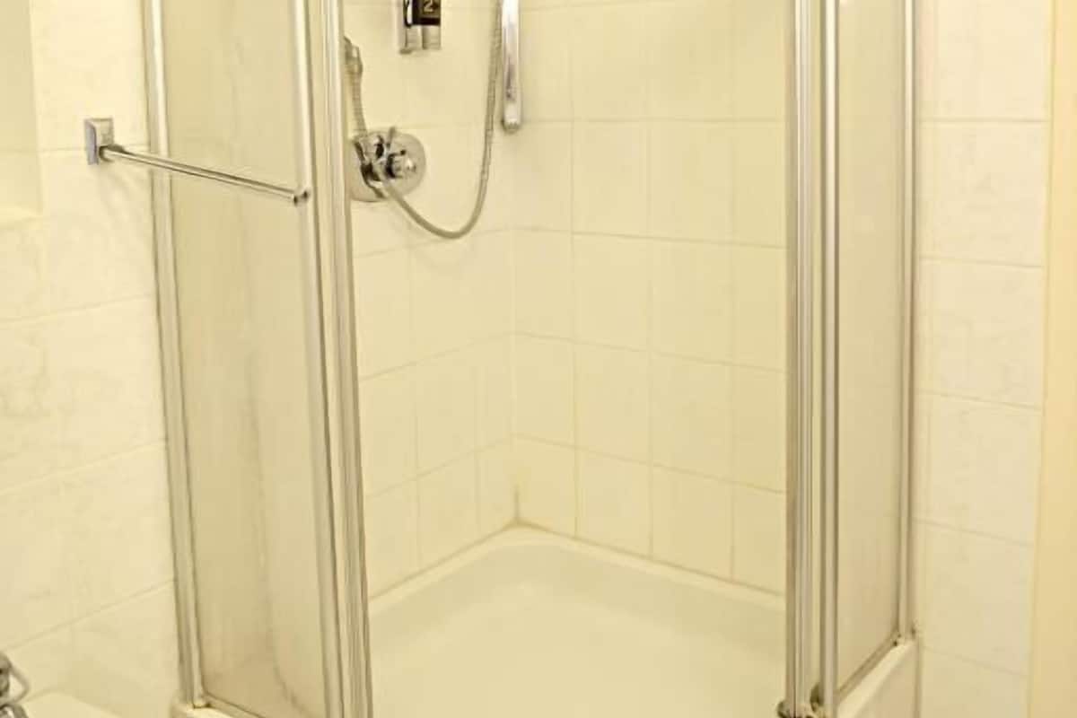A glass-enclosed shower with a handheld showerhead and a control panel.