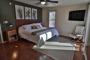Une chambre à coucher avec un lit, une table de chevet, une chaise, un téléviseur et des œuvres d’art accrochées au mur.