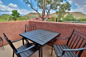 Une terrasse avec une table et des chaises, un mur à texture, et une vue sur un paysage vallonné avec des bâtiments visibles au loin.