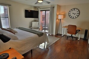 Une chambre d’hôtel équipée d’un lit, d’un bureau, d’une chaise, d’une télévision et d’une grande horloge murale.