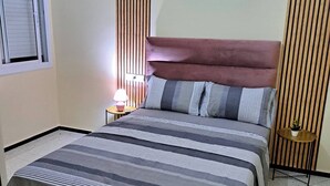 A bedroom with a large bed, a bedside table with a lamp, a small round table with a plant, and vertical wooden slats on the walls. - Atlas City Center Apartment (Fes)