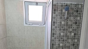 A bathroom with a toilet, a shower with patterned tiles, and a small window above the toilet. - Atlas City Center Apartment (Fes)