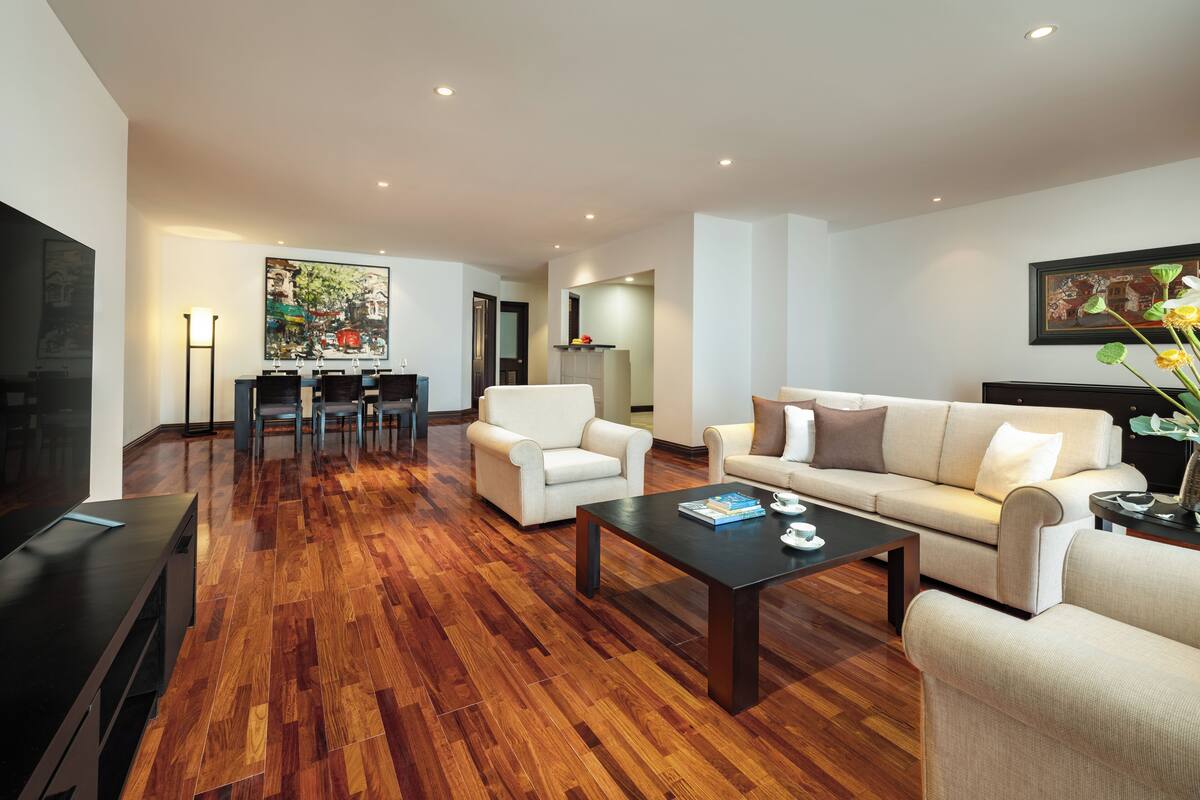 A modern living room with a wooden floor, a sofa, a coffee table, and a dining area with chairs and a table.