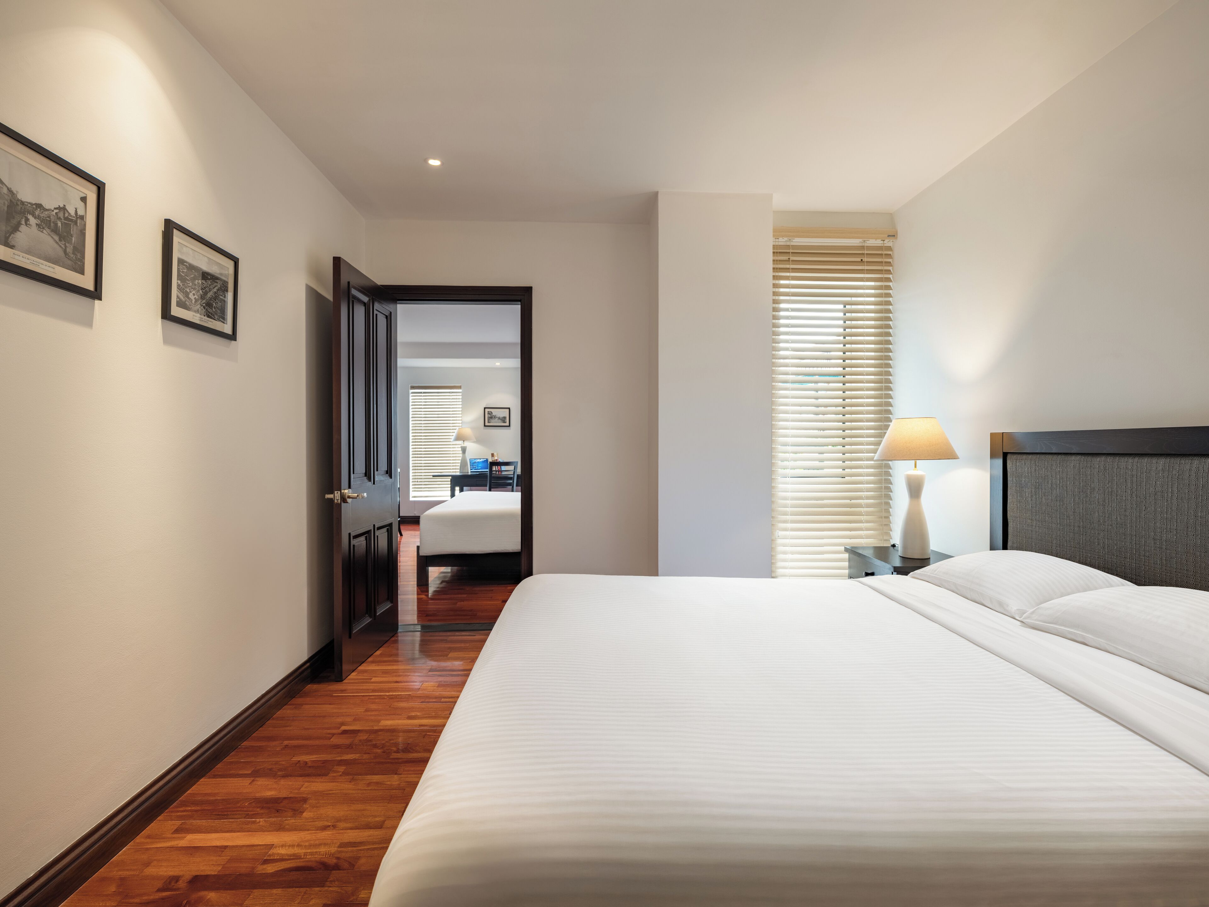 Une chambre d’hôtel avec un grand lit, une table de chevet avec une lampe, un plancher en bois et une porte donnant sur une autre pièce.