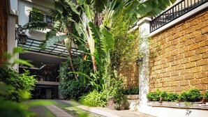 A courtyard with a cobblestone path, lush greenery, and a brick wall.