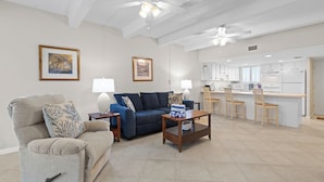 A modern living room with a sofa, armchairs, and a coffee table. There is a kitchen area with a bar and chairs.