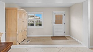 A hallway with a wooden cabinet, a white door, and a window with blinds.