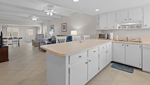 A spacious kitchen with white cabinets, a central island, and a dining area with a sofa and table.