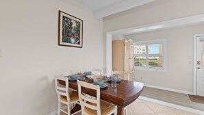 Un comedor con una mesa de madera, sillas blancas y un cuadro en la pared.
