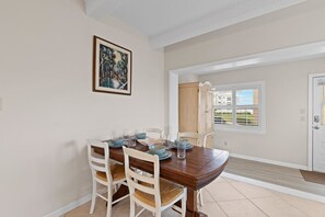 A dining area with a wooden table, white chairs, and a framed picture on the wall.
