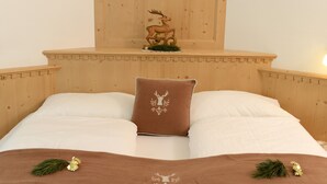 Una cama con cabecera marrón, ropa de cama blanca y un cojín decorativo con diseño de árbol.