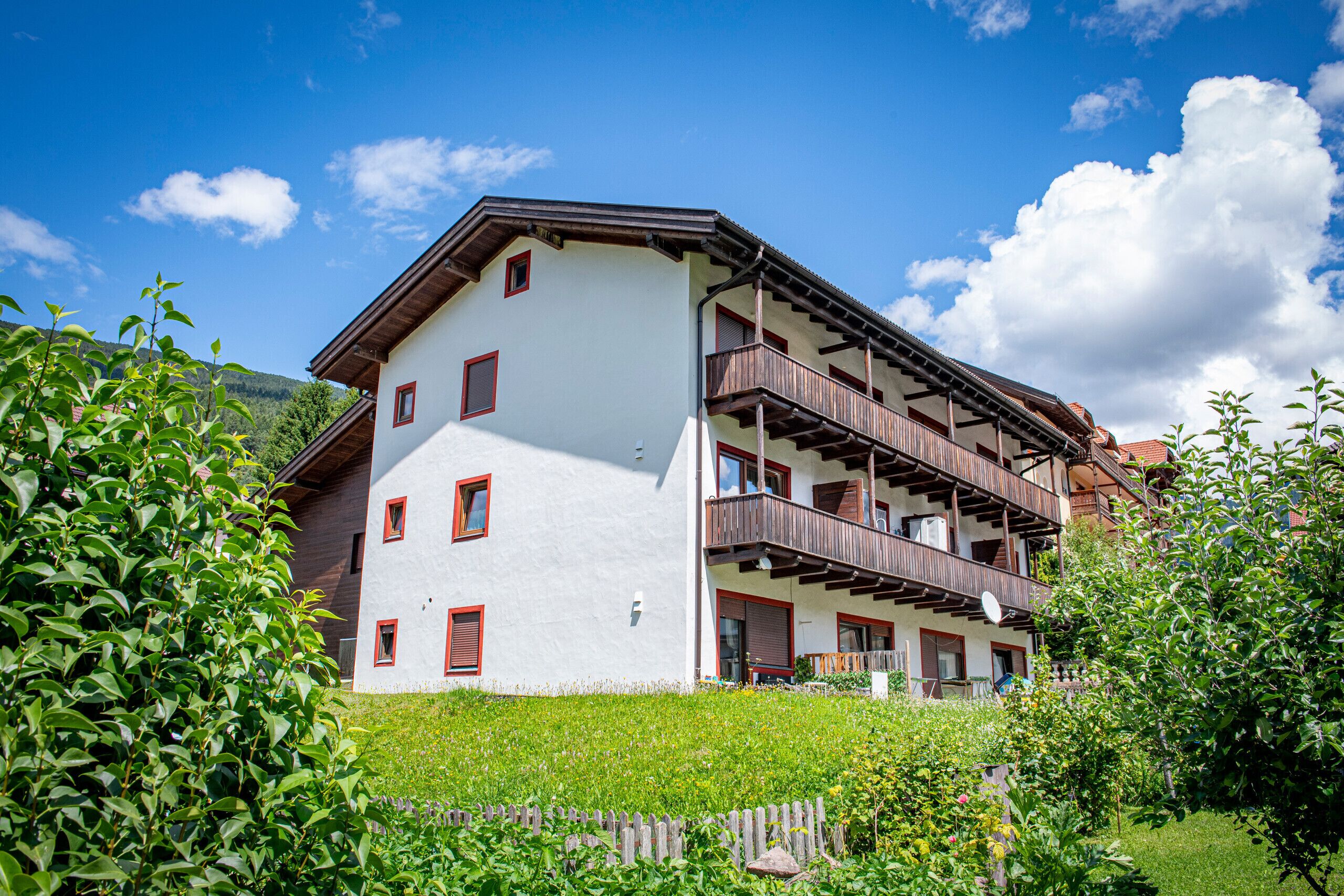 Un immeuble à plusieurs étages, doté de balcons et d’une façade blanche, avec une chaîne de montagnes en arrière-plan.