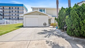 A residential building with a white garage, a covered driveway, and a well-maintained lawn.