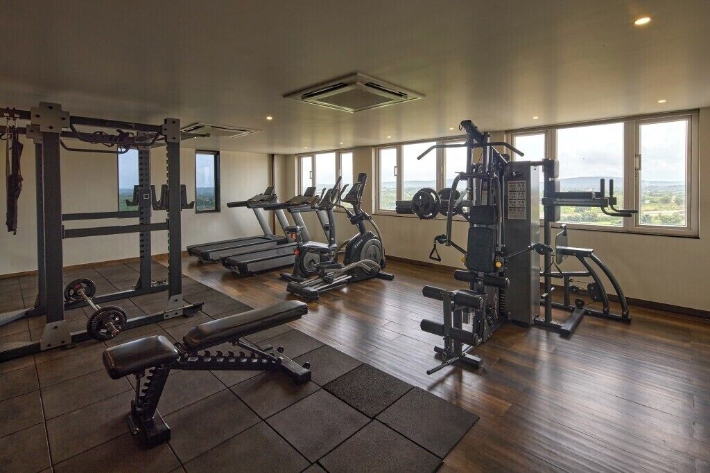 Un gimnasio con varios equipos de ejercicio, ventanas amplias y vistas al exterior.