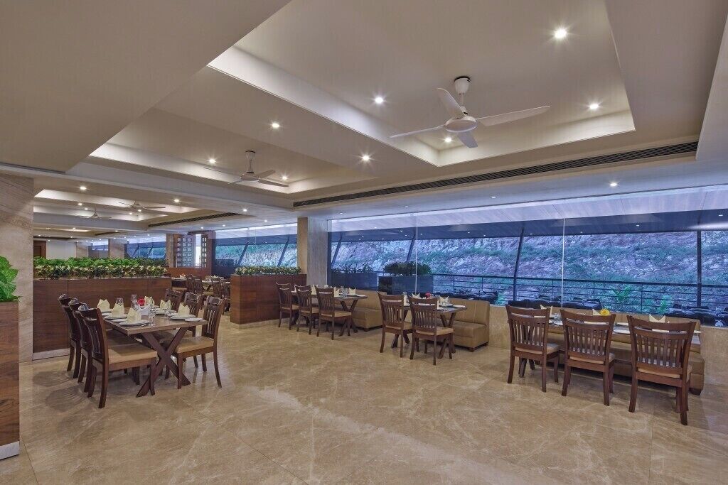 A spacious dining area with multiple tables and chairs, large windows offering a view, and ceiling fans.