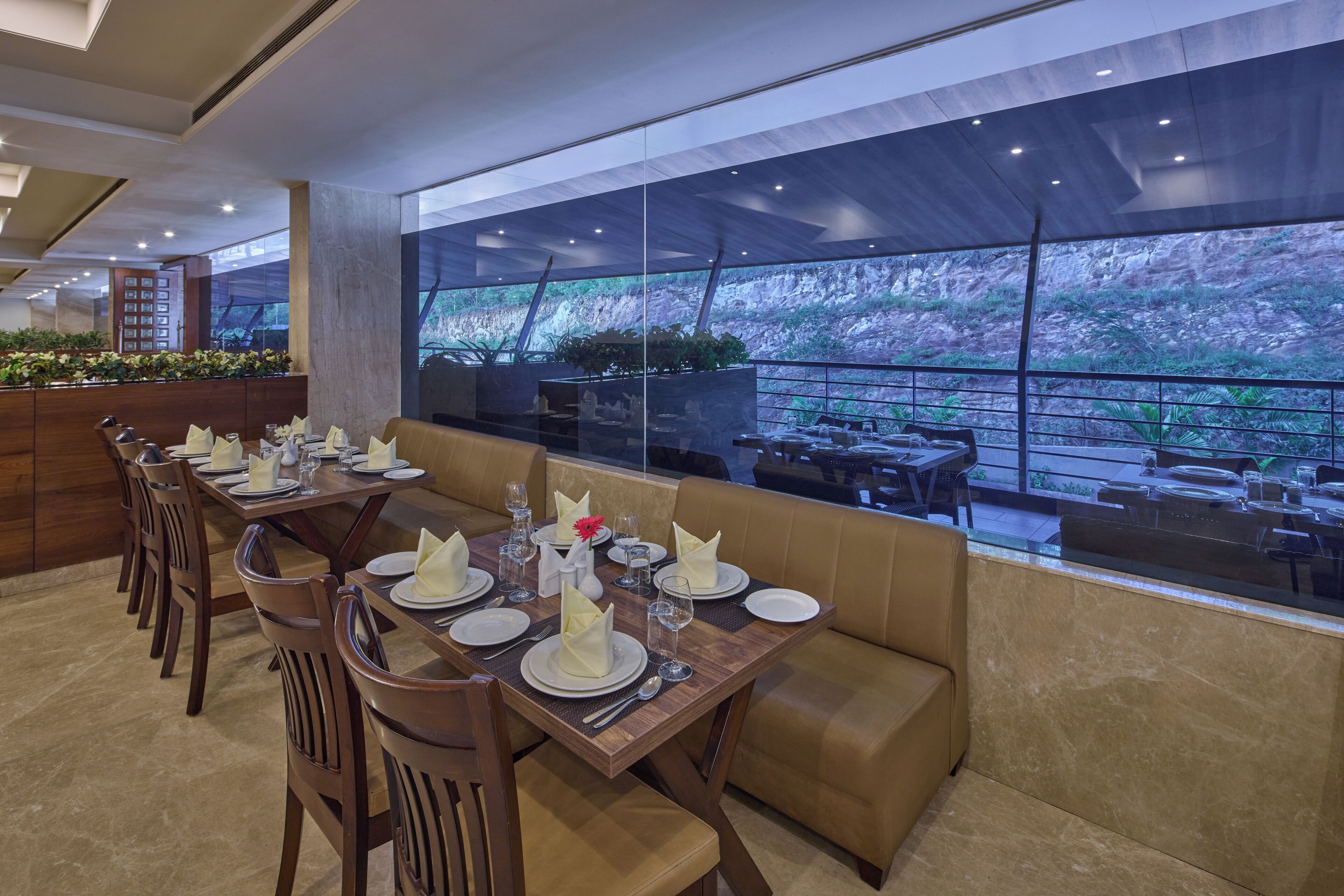 Un restaurante con una larga mesa de comedor dispuesta para una comida, ventanas amplias que ofrecen vistas a un paisaje rocoso y una decoración interior moderna.