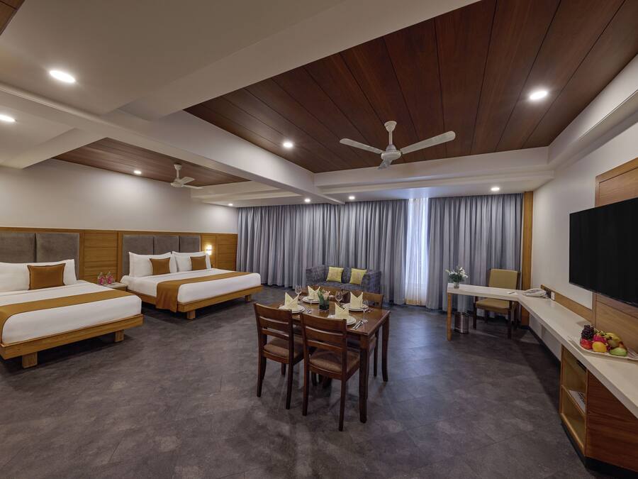 A hotel room with two beds, a dining area, a TV, and a ceiling fan.