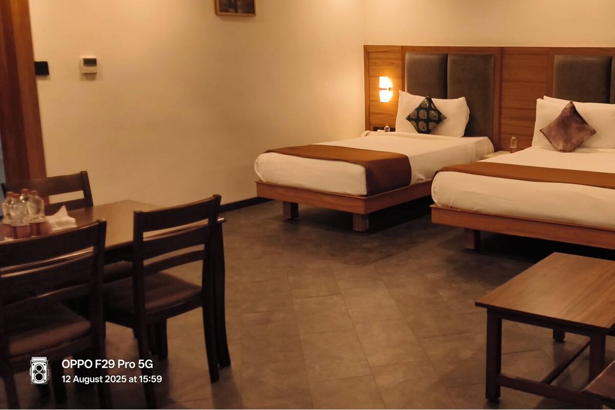 A hotel room with two beds, a dining table, chairs, and a small table.