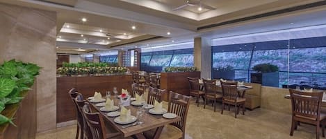 A restaurant with multiple dining tables and chairs, a ceiling fan, and a large window with a view.