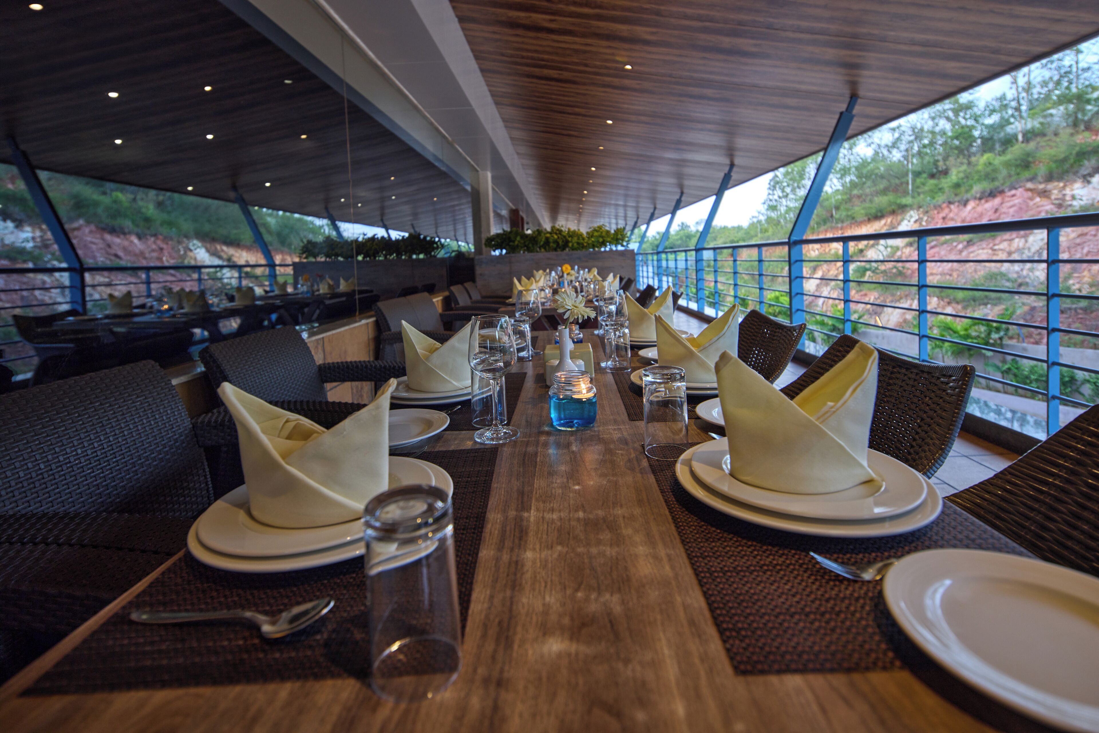 A restaurant with a long table set for dining, surrounded by chairs and a view of the outdoors.
