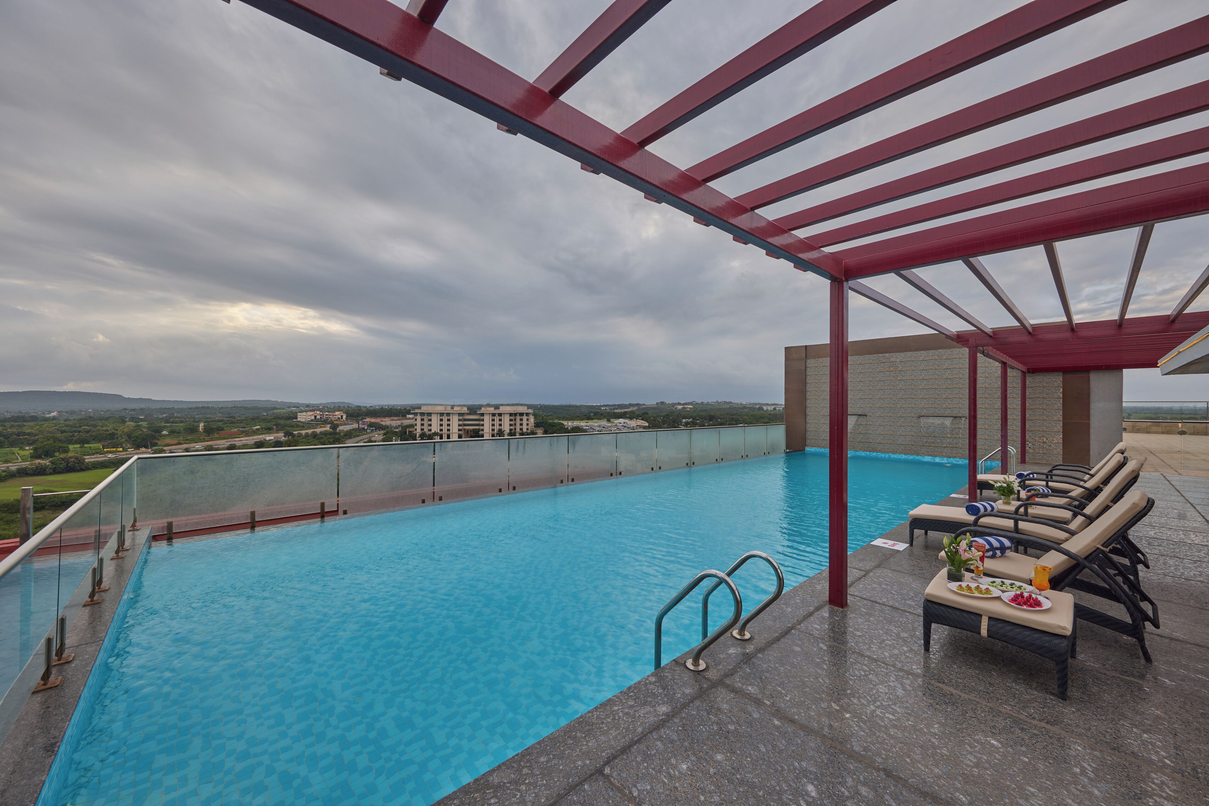 Una piscina en la azotea con agua azul cristalina, un pérgola roja y vistas a edificios lejanos.