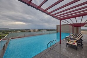 A rooftop pool with clear blue water, a red pergola, and a view of distant buildings. - Regenta Hubbali (Hubli)