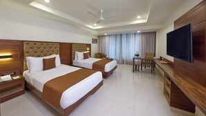 A hotel room with two beds, a desk, a chair, a television, and a ceiling fan. - Regenta Hubbali (Hubli)