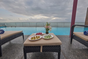 Mesa junto a la piscina con platos de comida y un jarrón de flores, con vista a una piscina.
